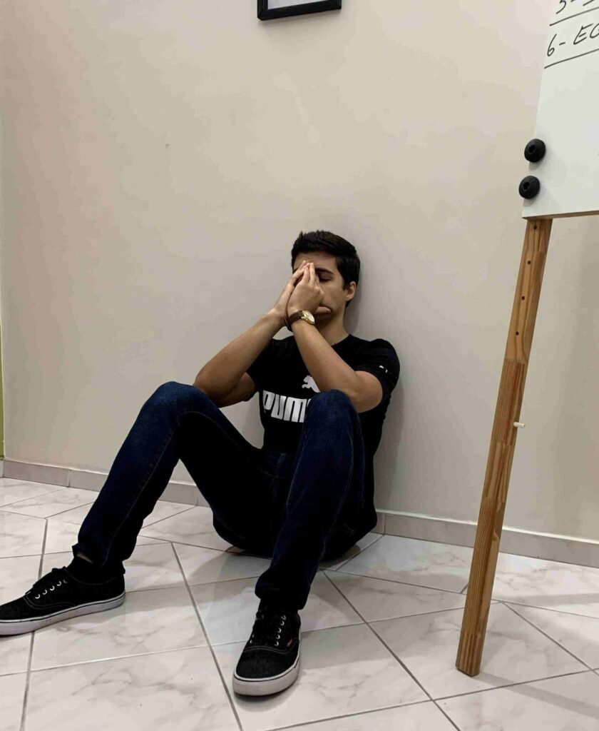 Meditação jovem sentado no chão com parede clara e quadro branco ao lado, expressão de reflexão e tranquilidade.