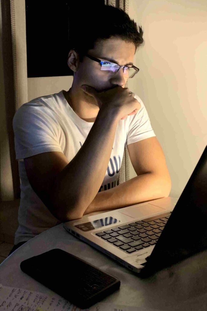 1. Jovem usando óculos frente a laptop, estudando ou trabalhando em casa com iluminação suave.