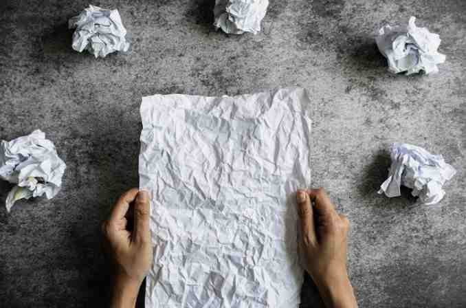 Rascunho de papel amassado com dúvidas e ideias ao redor, simbolizando criatividade e reflexão.