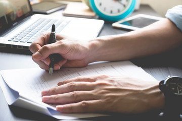 Escritório com computador e mãos escrevendo, ambiente de trabalho profissional.